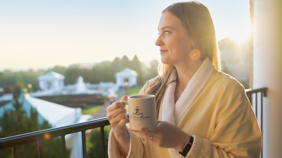 A woman in white robe with coffee looking over a balcony at The Spa at The Hotel Hershey.